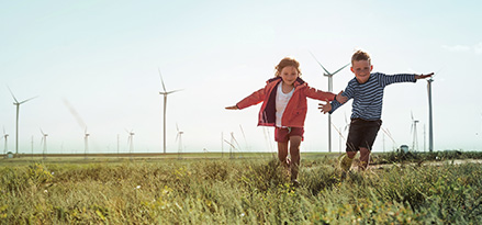 Deux enfants jouant dans un champ avec des éoliennes derrière eux