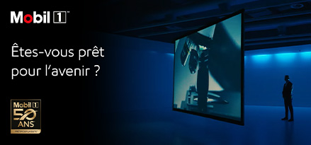 Un homme debout devant un grand écran, regardant un film, avec un logo Mobil 1 50 ans et le texte suivant : Are you ready for what s next ?